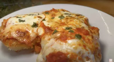 Delicious homemade chicken parmesan with melted cheese and tomato sauce on a white plate.
